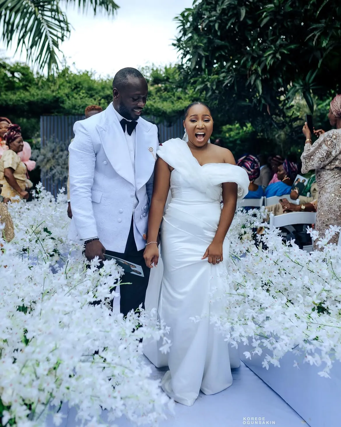 Bride Olufunmilade walking the aisle in a Bojamiley one shoulder white wedding dress at an outdoor ceremony